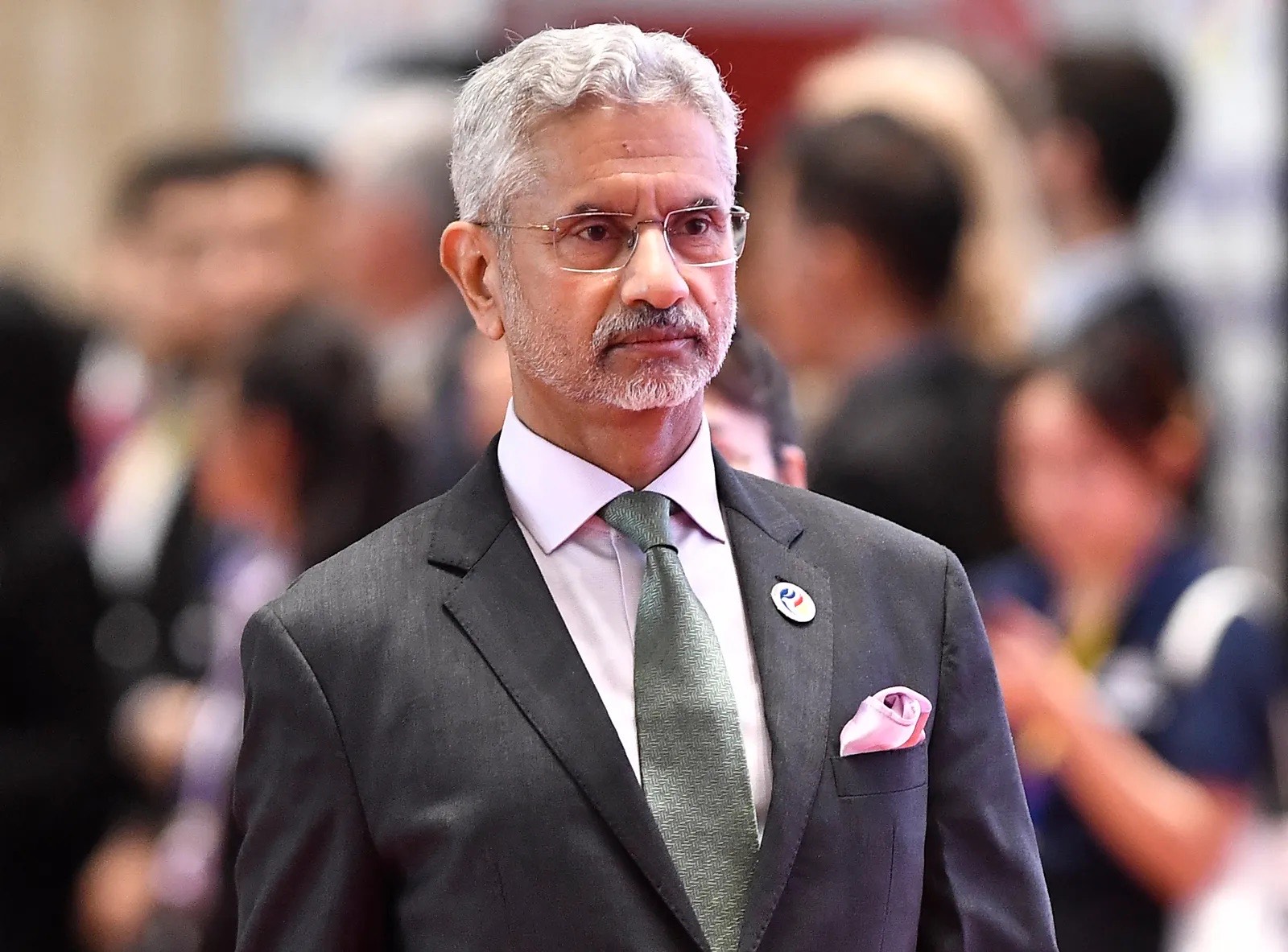 Dr. S. Jaishankar in a grey suit and green tie arriving at a conference venue, with delegates in the background