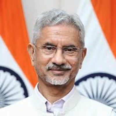 Head-and-shoulders portrait of Dr. S. Jaishankar smiling, in front of Indian flags