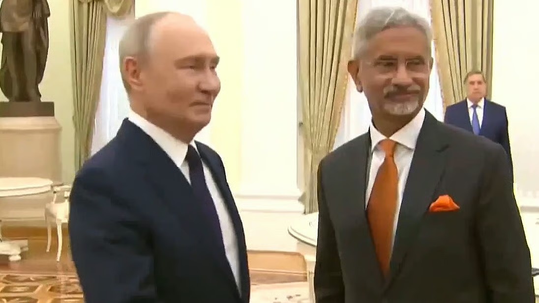 Dr. S. Jaishankar in a grey suit and orange tie at a formal meeting in an ornate hall, beside a host