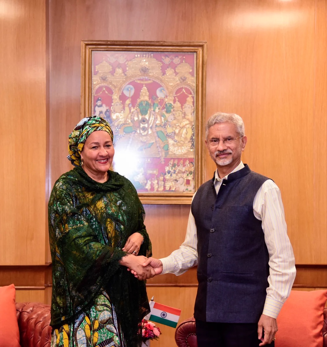 Dr. S. Jaishankar shaking hands with a visiting dignitary in a green patterned dress, in front of a framed traditional painting