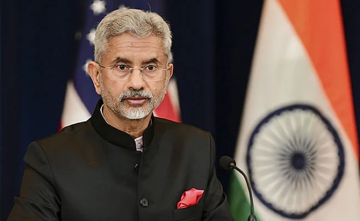 Dr. S. Jaishankar in a dark bandhgala speaking at a press engagement in front of US and Indian flags