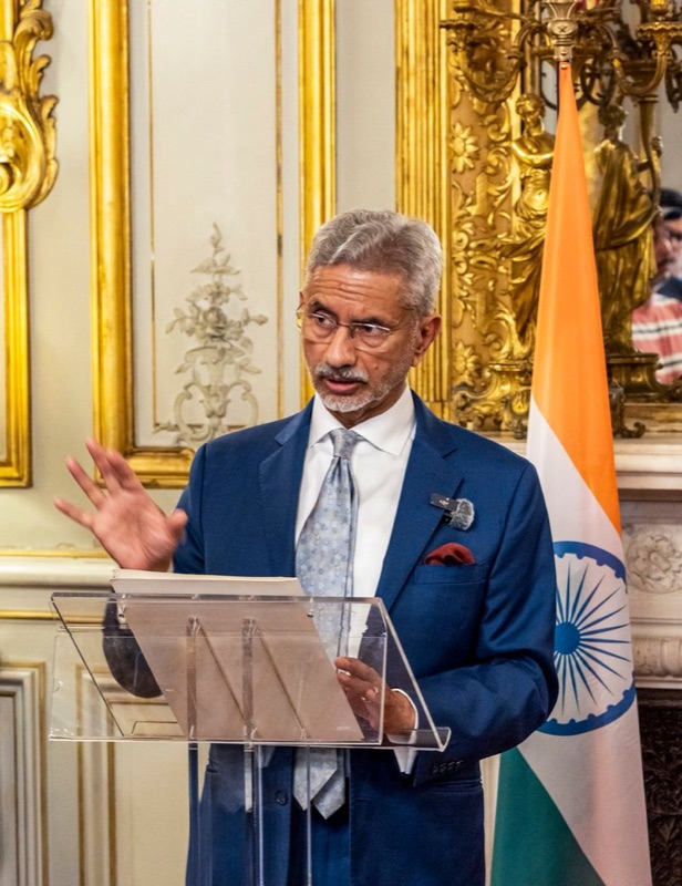 Dr. S. Jaishankar speaking at a transparent lectern in a gilded room beside the Indian flag